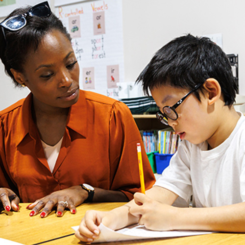 Photo of a teacher at a desk with their middle school student while they work on a problem